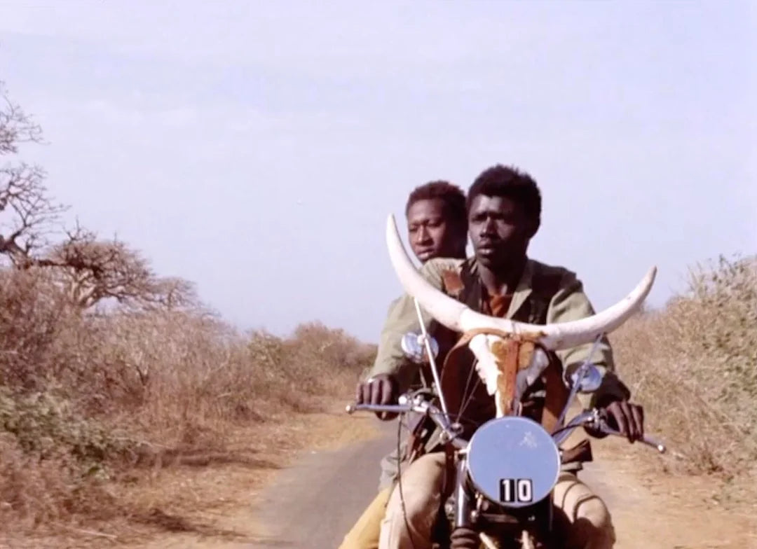 Motorcycle on road with front number plate and two riders riding forward